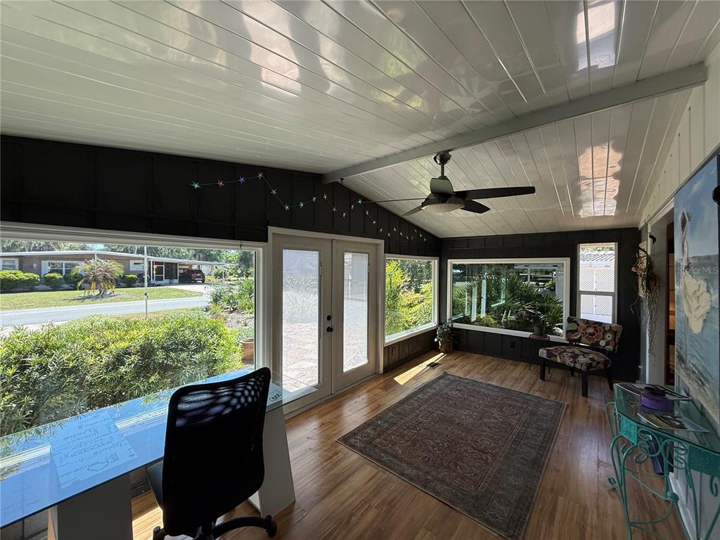 A sunroom with wood-look flooring, a ceiling fan, large windows, and a glass-topped desk — 9 S BOBWHITE ROAD, WILDWOOD, FL