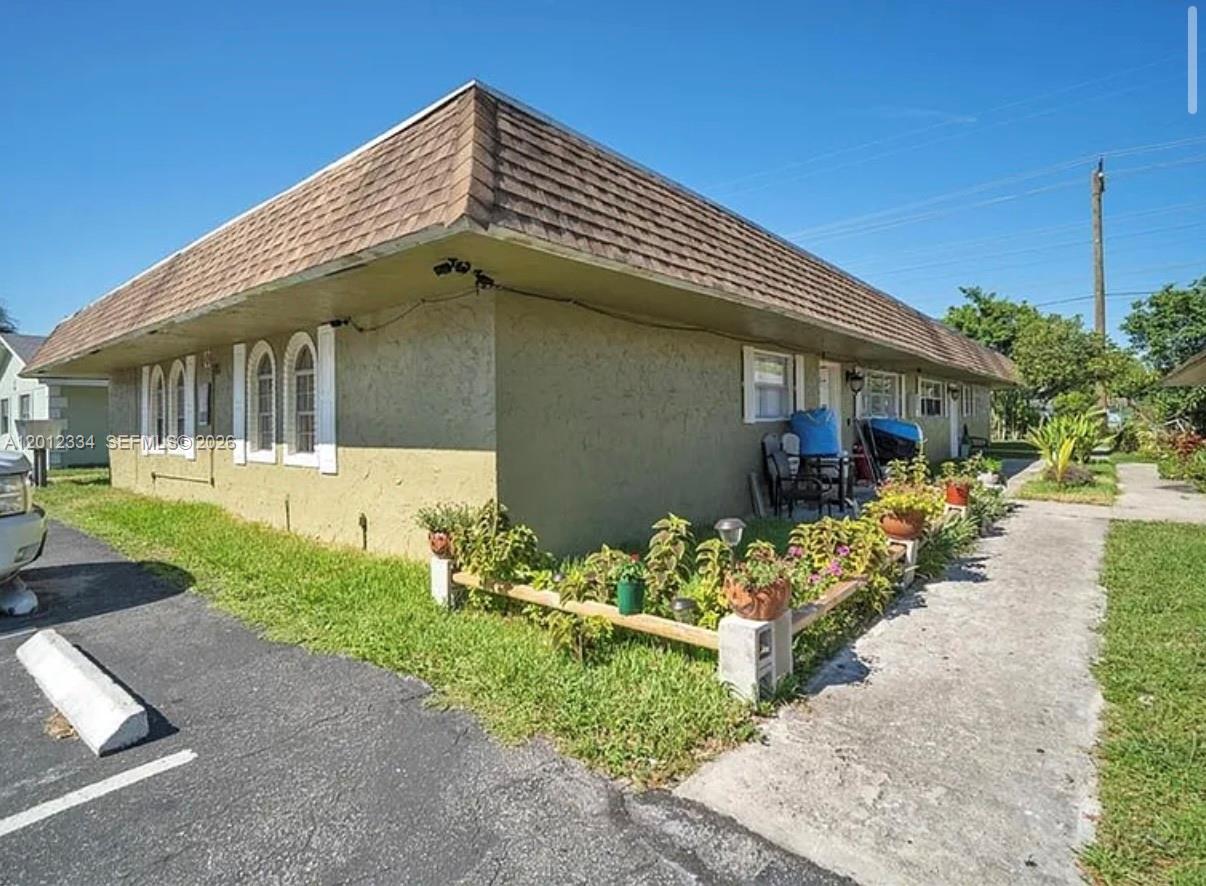 A low-slung, single-story apartment building with a brown shingled roof and a small garden — 581 Kathy Ln # D, Margate FL 33068, MARGATE, FL