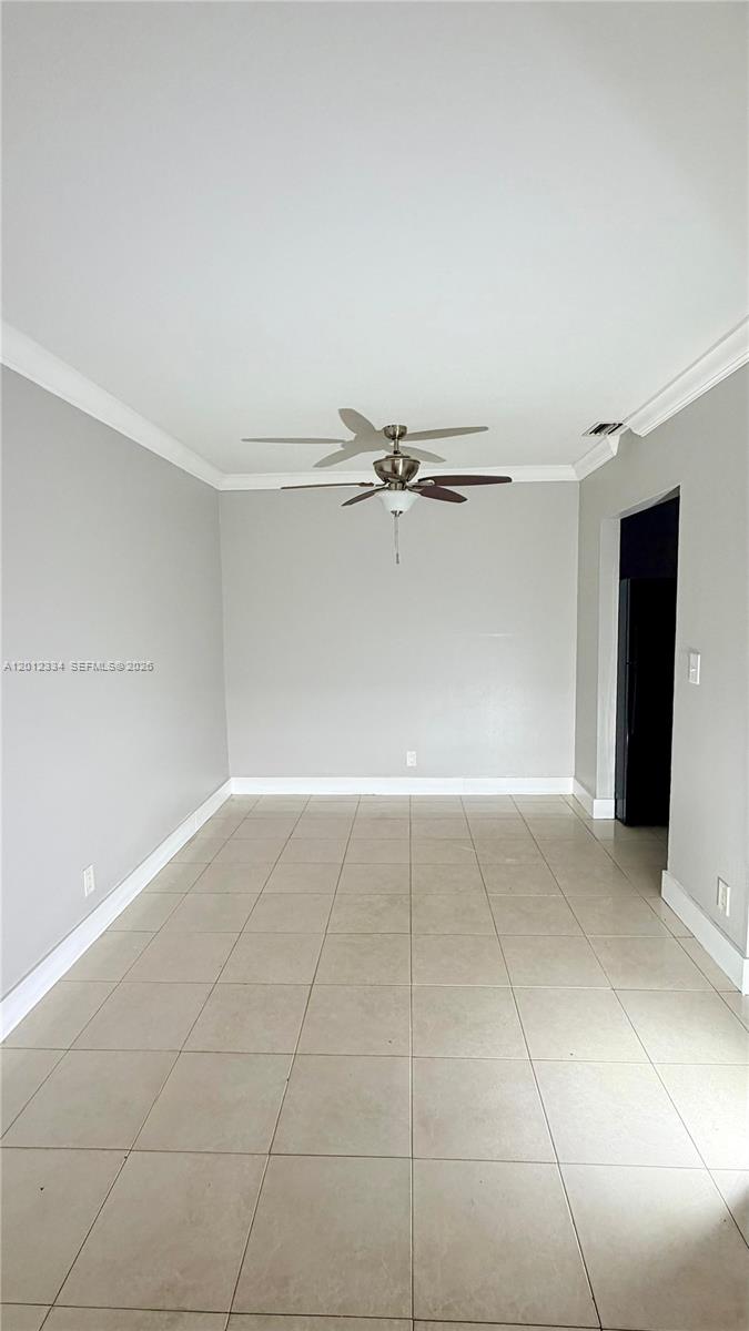 An empty room features light gray walls, white crown molding, and large beige floor tiles — 581 Kathy Ln # D, Margate FL 33068, MARGATE, FL