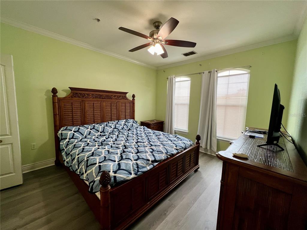 A bedroom features a wooden bed frame, light green walls, and wood-look flooring — 2713 VIA MURANO UNIT 232, CLEARWATER, FL