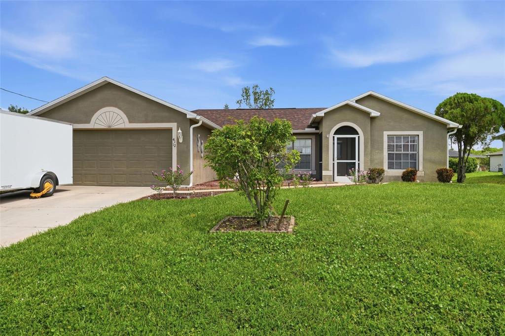 A single-story house with a tan stucco exterior, a two-car garage, and a front lawn — 4112 10TH STREET W, LEHIGH ACRES, FL