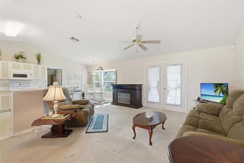 A living room with beige carpet, a ceiling fan, a fireplace, and an adjacent kitchen — 4112 10TH STREET W, LEHIGH ACRES, FL