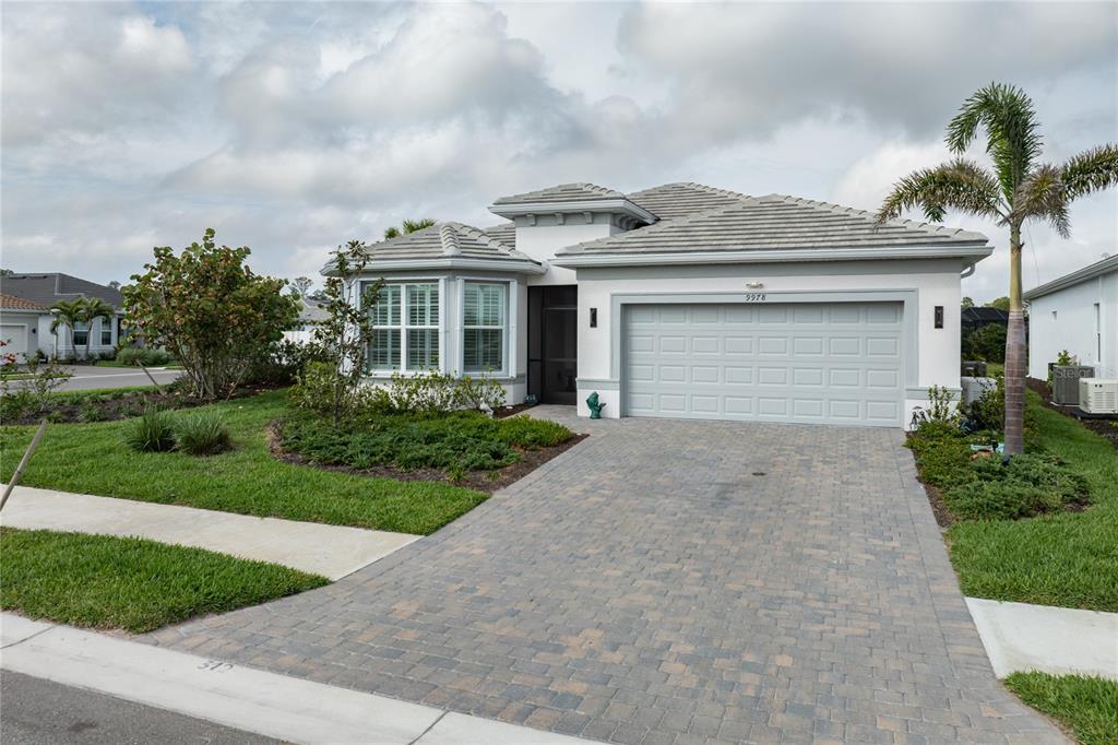 A single-story house with a gray tile roof, white stucco walls, and a paver driveway — 9978 BRIGHT WATER DRIVE, ENGLEWOOD, FL