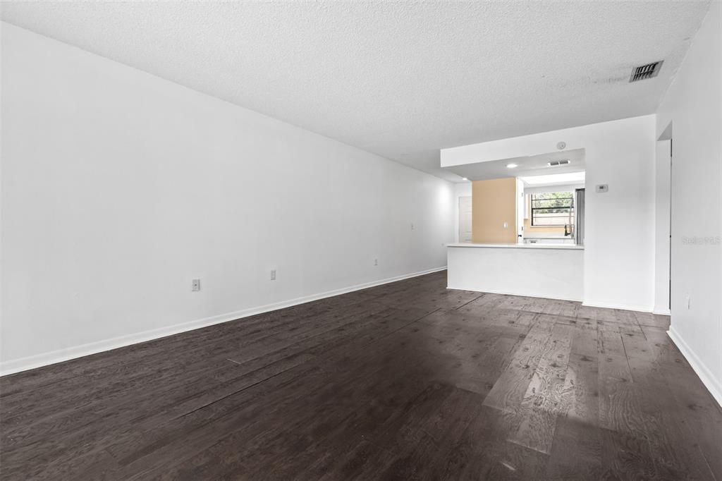 An empty living room with dark wood-look flooring and a pass-through to the kitchen — 6045 TOPHER TRAIL UNIT C-24, MULBERRY, FL