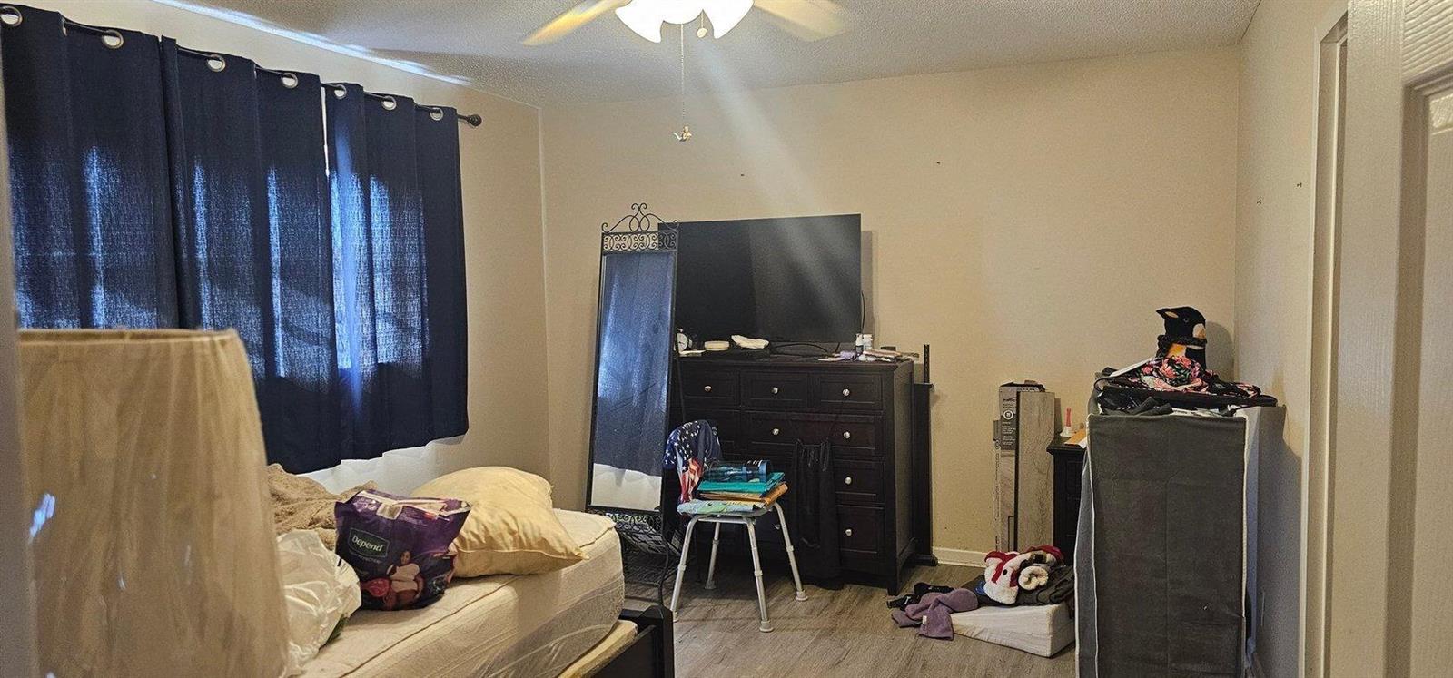 A bedroom features a bed, a dark wood dresser with a television, and blue curtains — 14721 Bonaire Boulevard # 309, Delray Beach FL 33446, DELRAY BEACH, FL