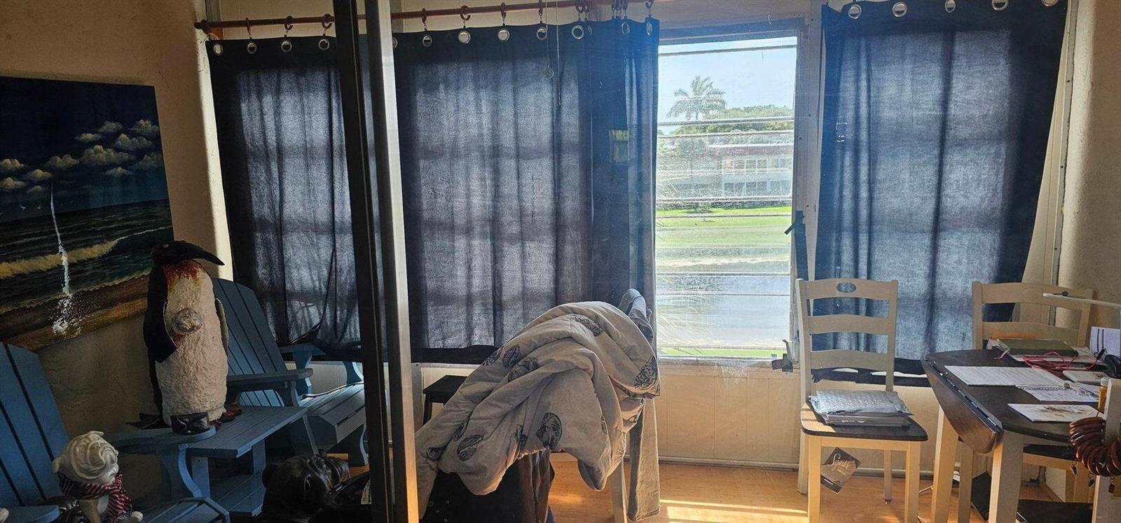 A sunroom features dark curtains, blue chairs, a dining table, and a view of greenery — 14721 Bonaire Boulevard # 309, Delray Beach FL 33446, DELRAY BEACH, FL