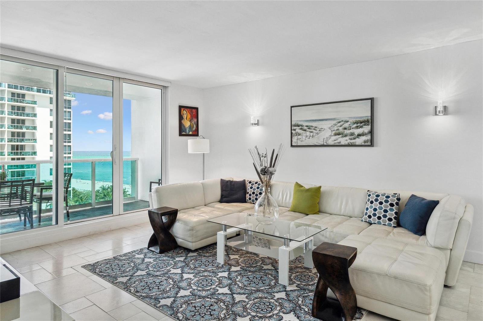 A living room features a white sectional sofa, a glass coffee table, and ocean views — 2301 Collins Avenue # 1015, Miami Beach FL 33139, MIAMI BEACH, FL