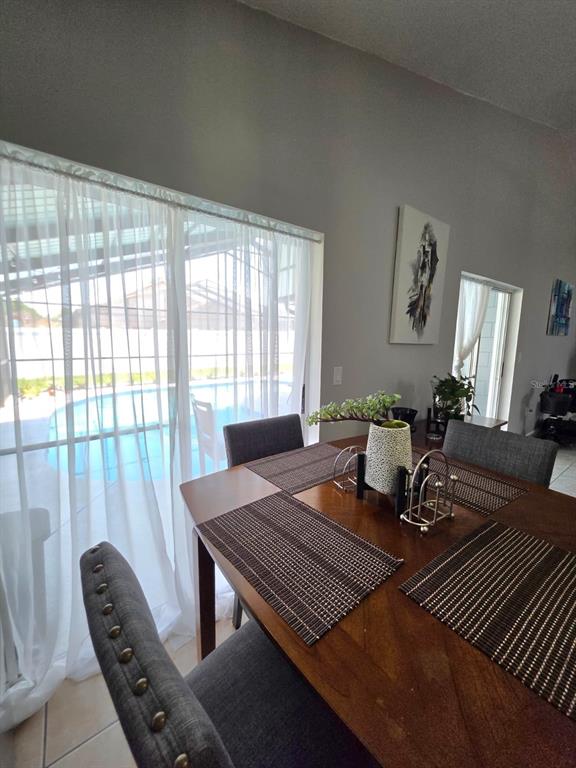A dining area features a wooden table, grey upholstered chairs, and sliding doors overlooking a pool — 763 COUNTRY WOODS CIRCLE, KISSIMMEE, FL