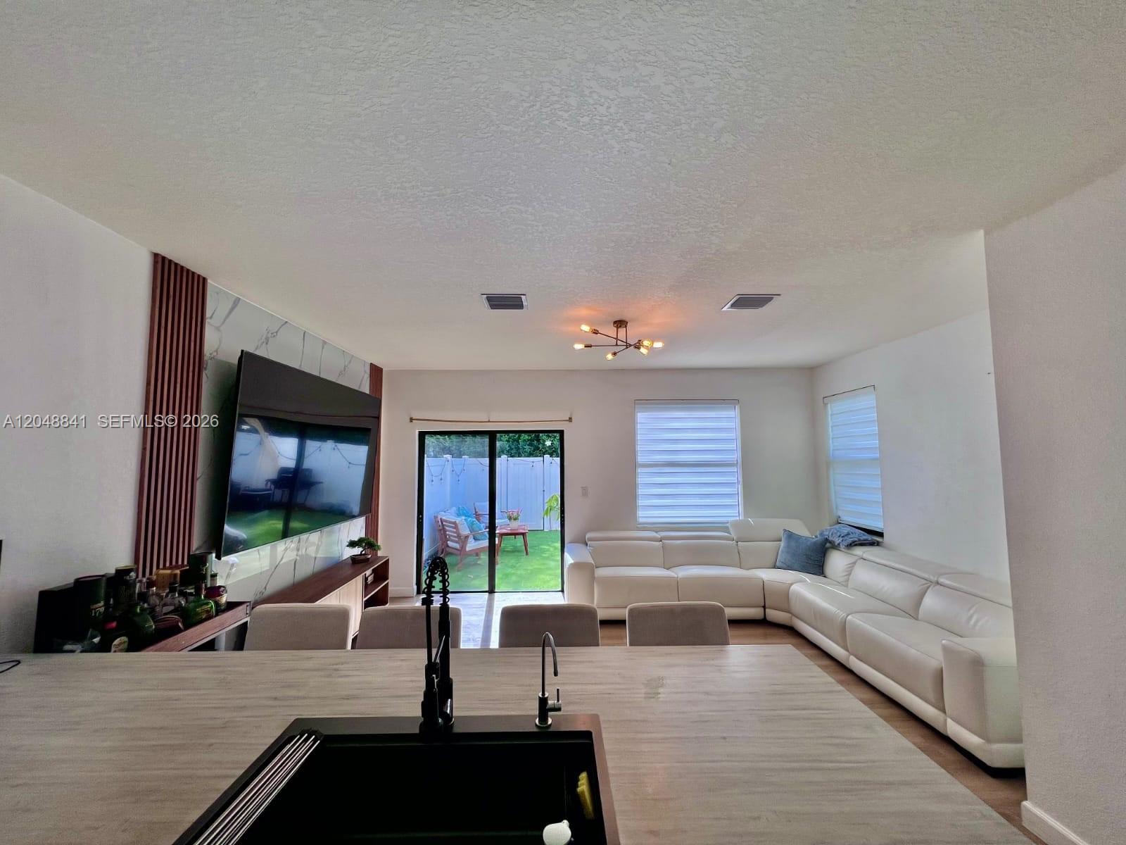 A kitchen island overlooks a living room with a white sectional and sliding glass doors — 10939 W 32nd Ln, Hialeah FL 33018, HIALEAH, FL