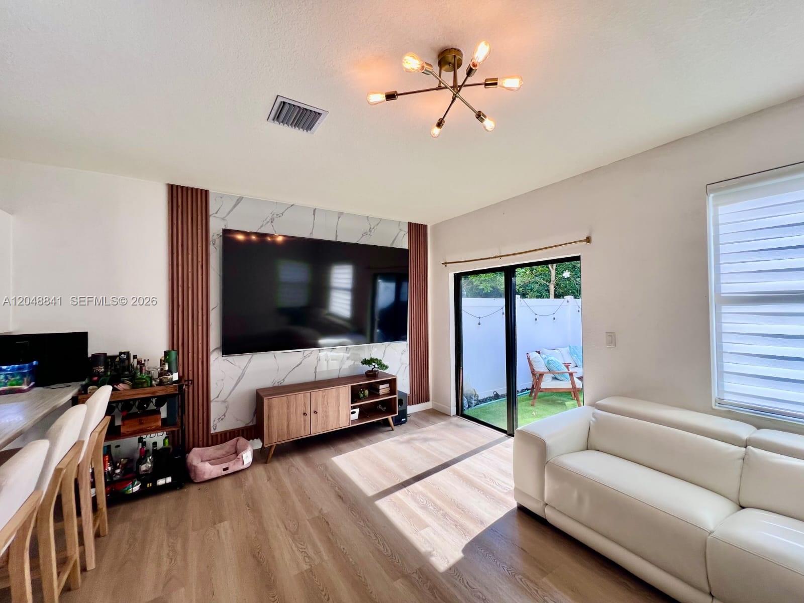 A living room features a marble-accented media wall, wood-look flooring, and a sliding glass door — 10939 W 32nd Ln, Hialeah FL 33018, HIALEAH, FL