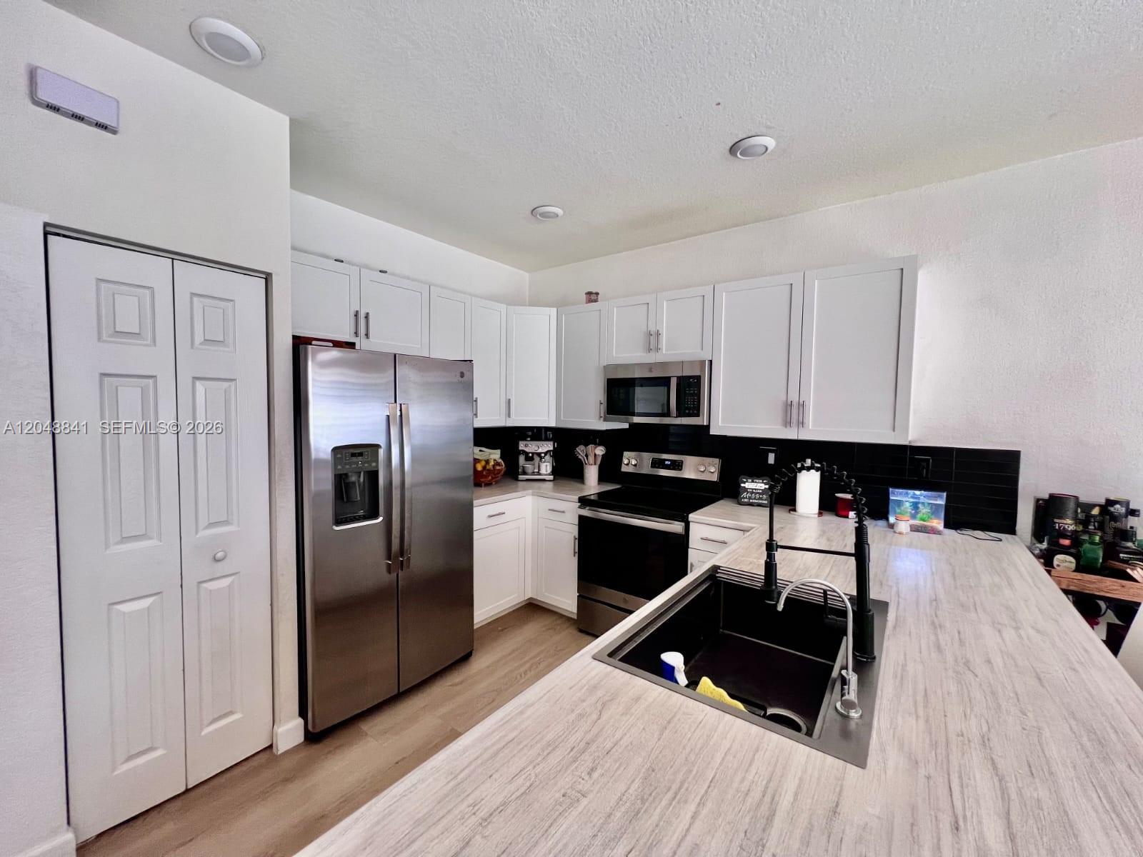 A kitchen features white cabinets, stainless steel appliances, a black backsplash, and a wood-look countertop — 10939 W 32nd Ln, Hialeah FL 33018, HIALEAH, FL