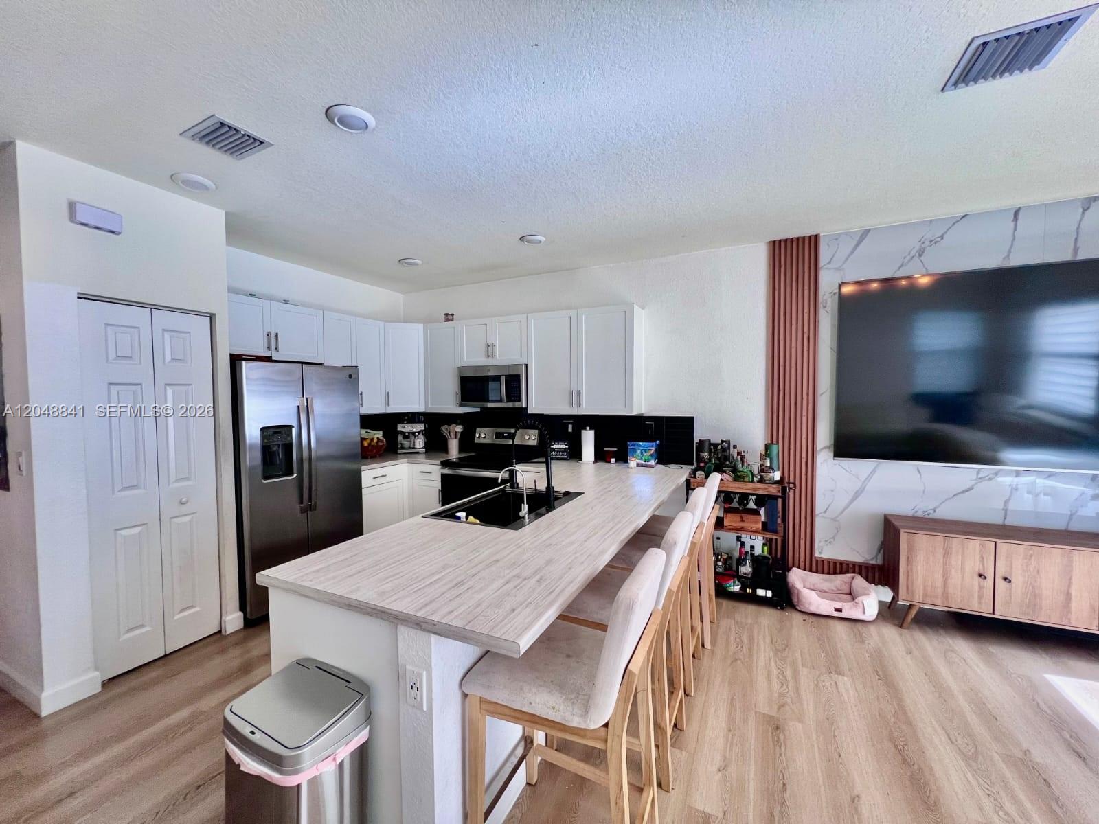 A kitchen features white cabinets, a wood-look island with bar seating, and stainless steel appliances — 10939 W 32nd Ln, Hialeah FL 33018, HIALEAH, FL