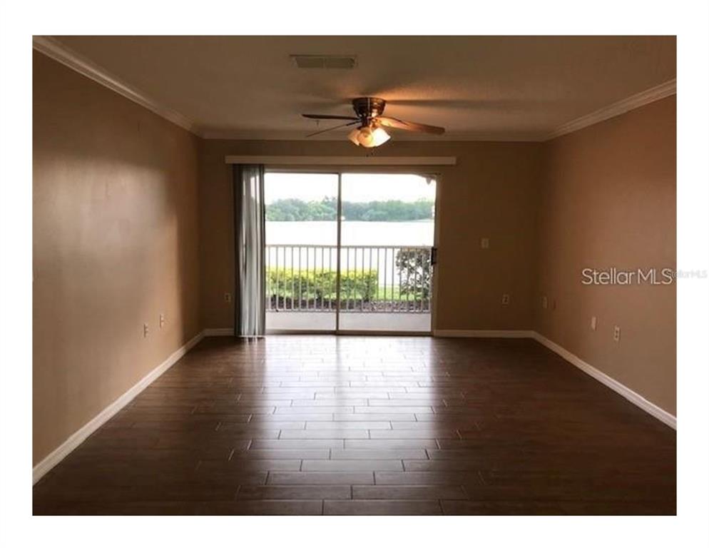 An empty living room features dark wood-look tile flooring, beige walls, and a sliding glass door — 1909 SUMMER CLUB APT 115 DRIVE UNIT 115, OVIEDO, FL