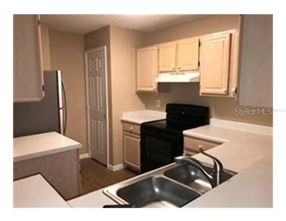 A kitchen features light-colored cabinets, white countertops, a black stove, and a double-basin sink — 1909 SUMMER CLUB APT 115 DRIVE UNIT 115, OVIEDO, FL