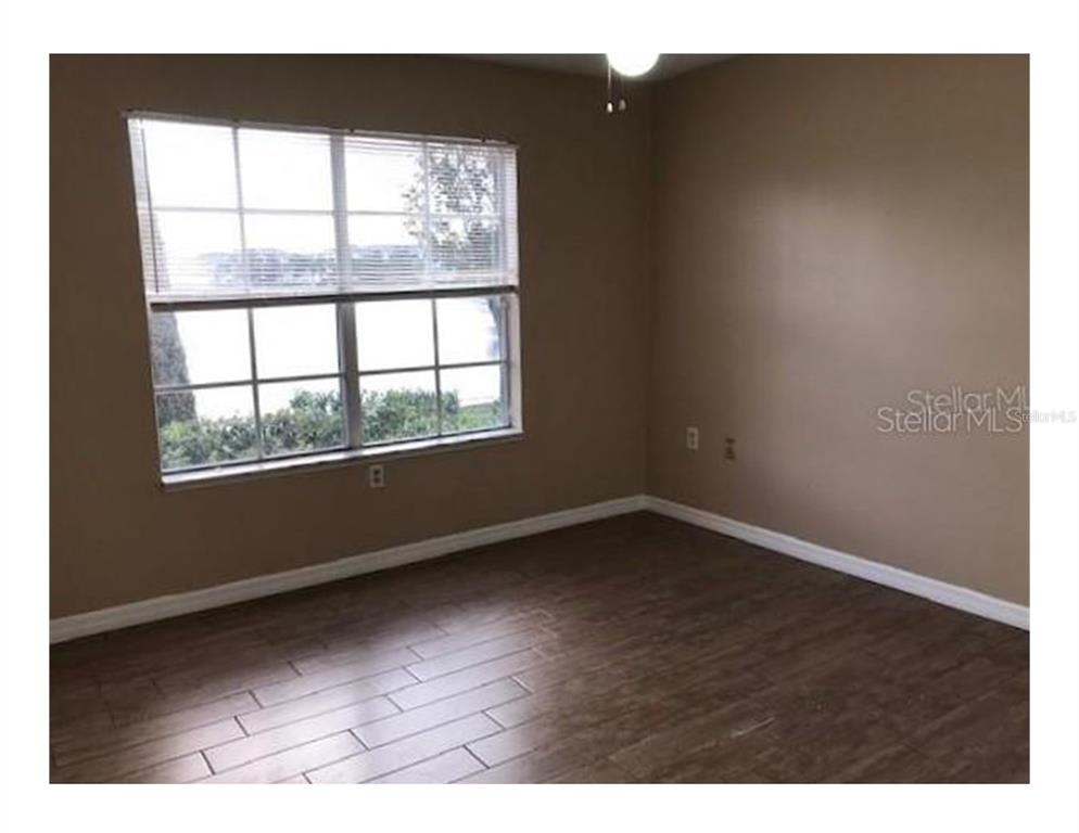 An empty bedroom features wood-look tile flooring, beige walls, and a window with blinds — 1909 SUMMER CLUB APT 115 DRIVE UNIT 115, OVIEDO, FL