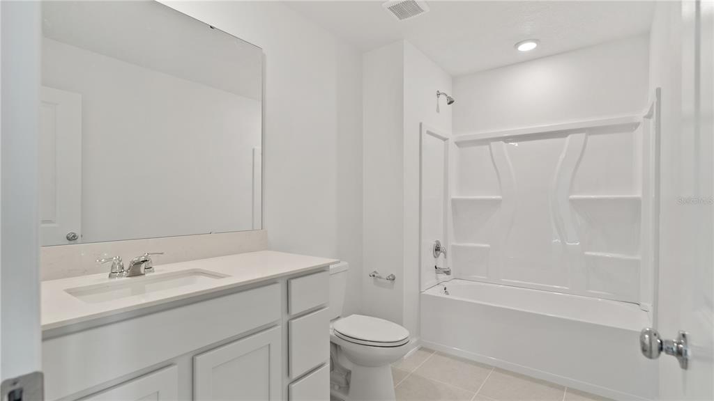 A bright bathroom features a white vanity, a toilet, and a tub-shower combination — 2497 HALLOW GARDEN ROAD, EUSTIS, FL