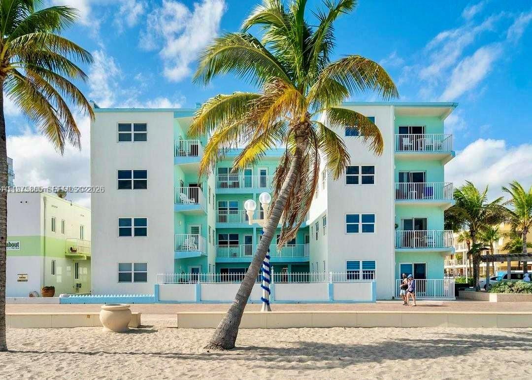 A multi-story, light blue and white apartment building stands behind a sandy beach with palm trees — 2600 N Surf Rd # 403, Hollywood FL 33019, HOLLYWOOD, FL