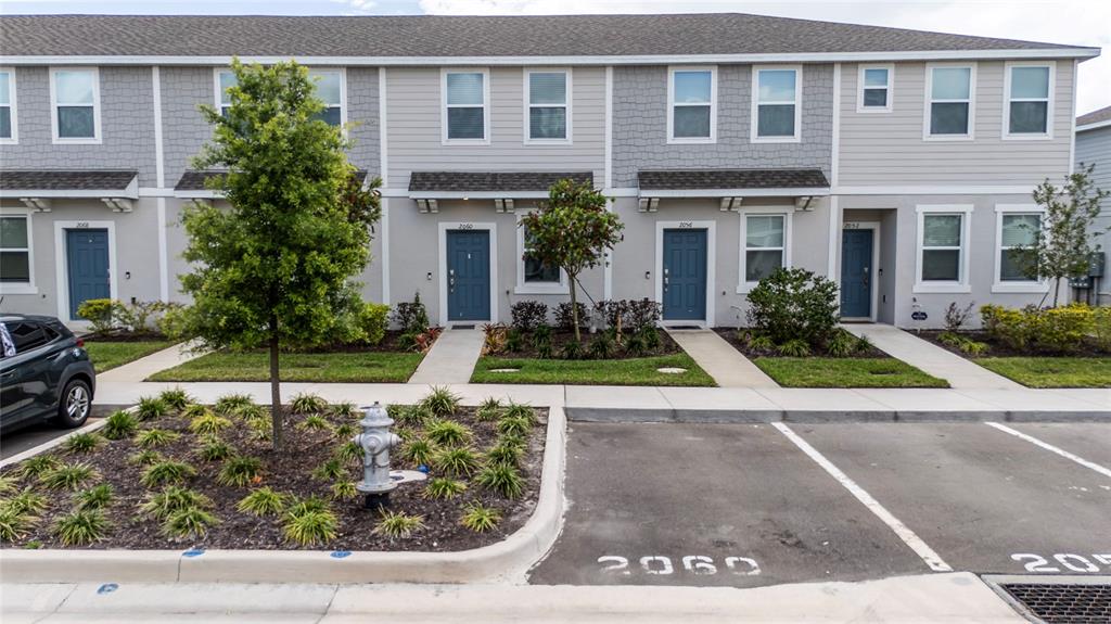 A row of two-story townhouses features gray siding, blue front doors, and a parking area — 2060 VIEWFINDER STREET, KISSIMMEE, FL