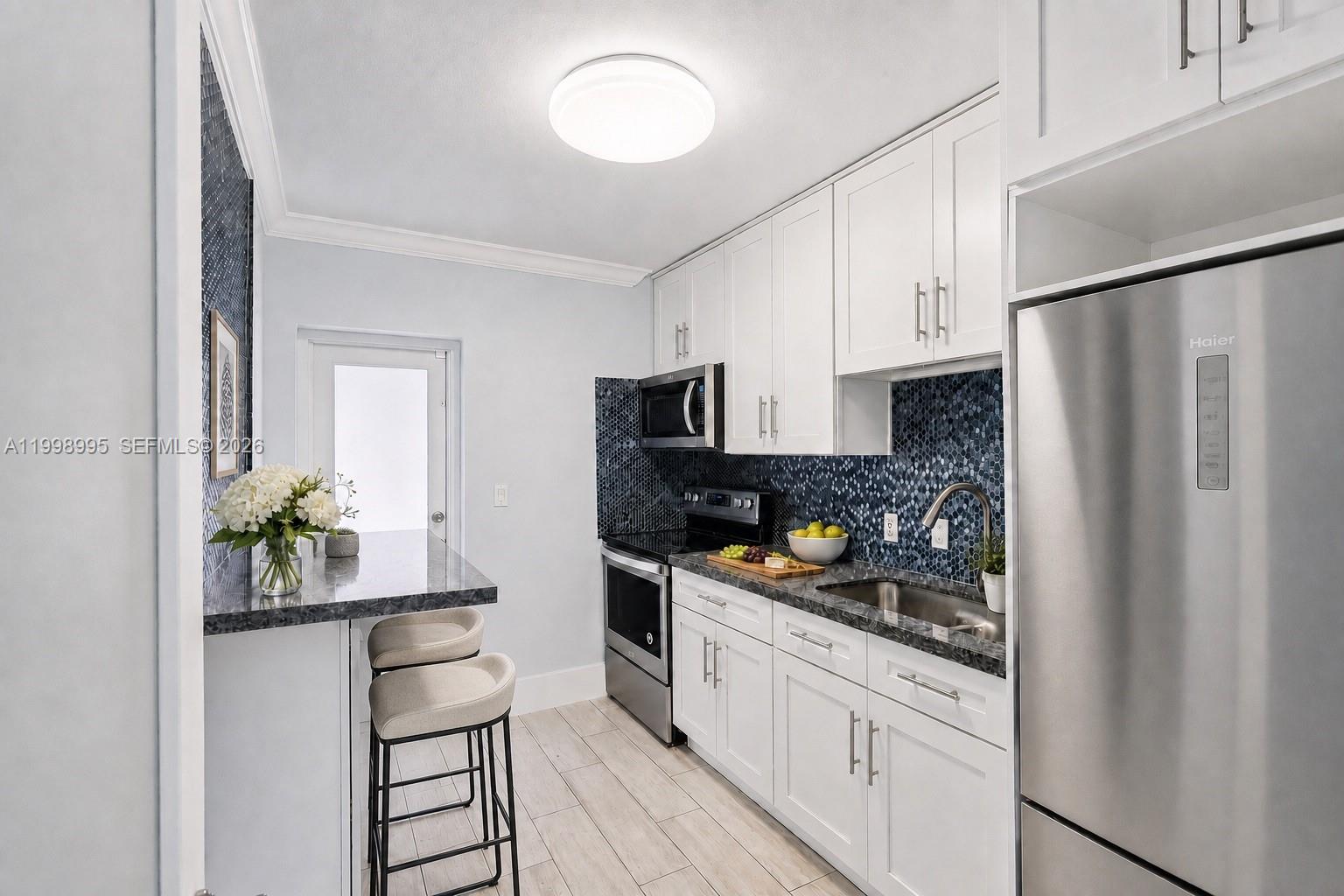 A kitchen features white cabinets, stainless steel appliances, a dark countertop, and blue mosaic backsplash — 1682 NE 124th Ln, North Miami FL 33181, NORTH MIAMI, FL