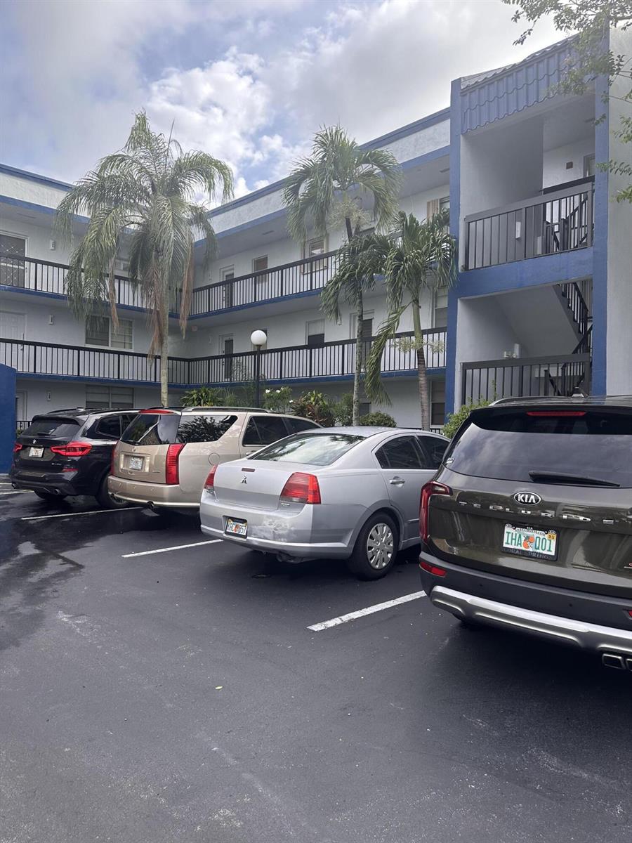 A multi-story apartment building exterior with a parking lot containing four parked vehicles — 3090 Holiday Springs Boulevard # 310, Margate FL 33063, MARGATE, FL