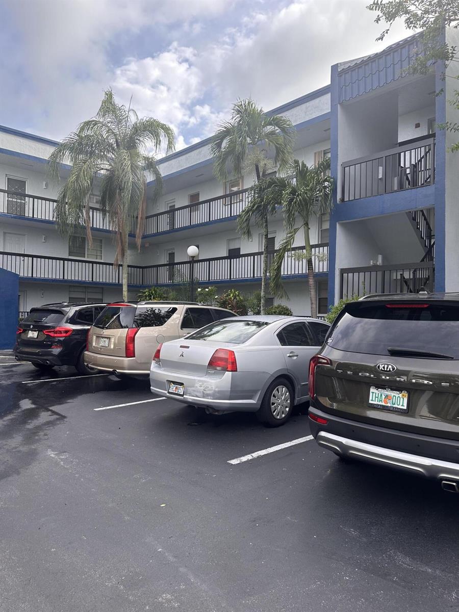 A parking lot sits in front of a multi-story apartment building with palm trees — 3090 Holiday Springs Boulevard # 310, Margate FL 33063, MARGATE, FL