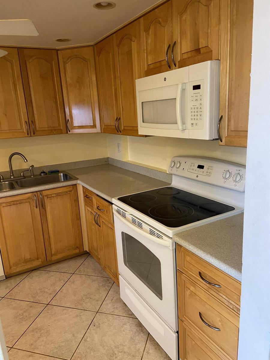 A kitchen with wooden cabinets, white appliances, and tiled flooring — 3090 Holiday Springs Boulevard # 310, Margate FL 33063, MARGATE, FL