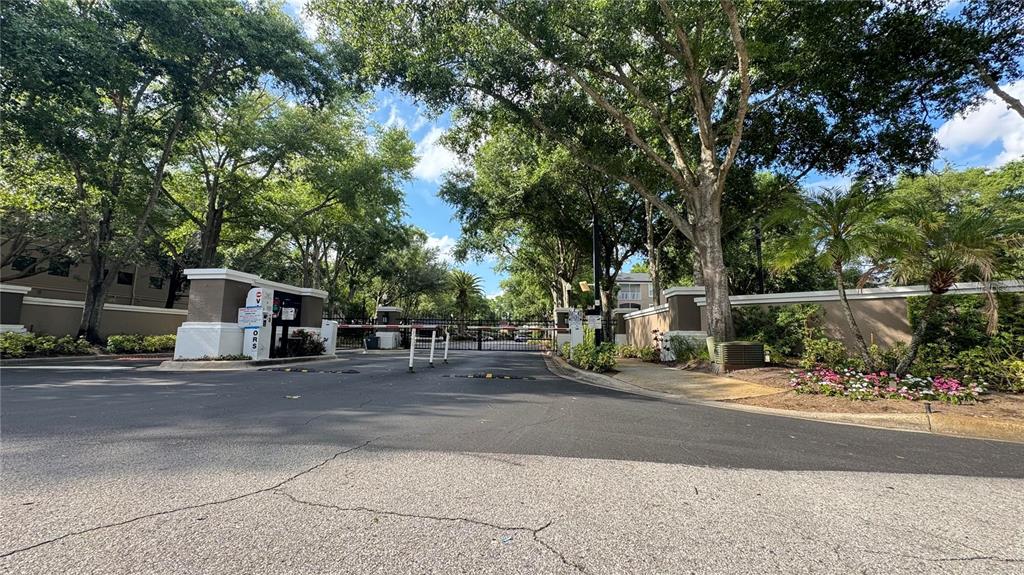 A gated entrance to a residential community features a security booth and mature trees — 7123 YACHT BASIN AVENUE UNIT 312, ORLANDO, FL