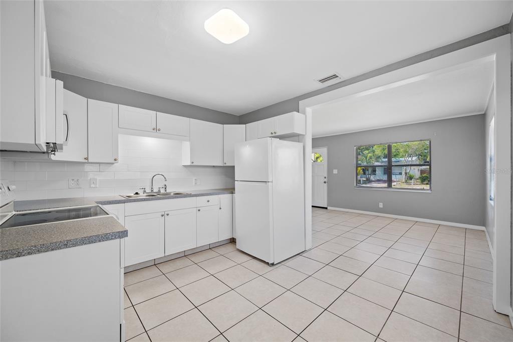 A kitchen with white cabinets, a white refrigerator, and tiled floors opens into a living area — 3246 20TH AVENUE S, ST PETERSBURG, FL