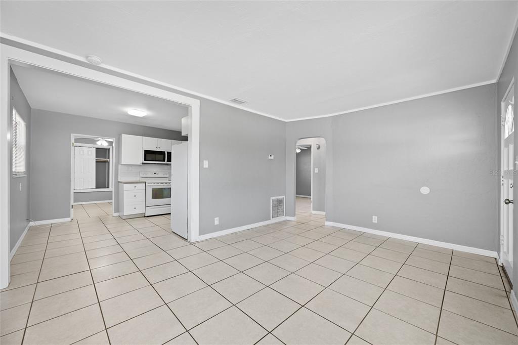 A living area with light gray walls and beige tile flooring leads into a kitchen — 3246 20TH AVENUE S, ST PETERSBURG, FL