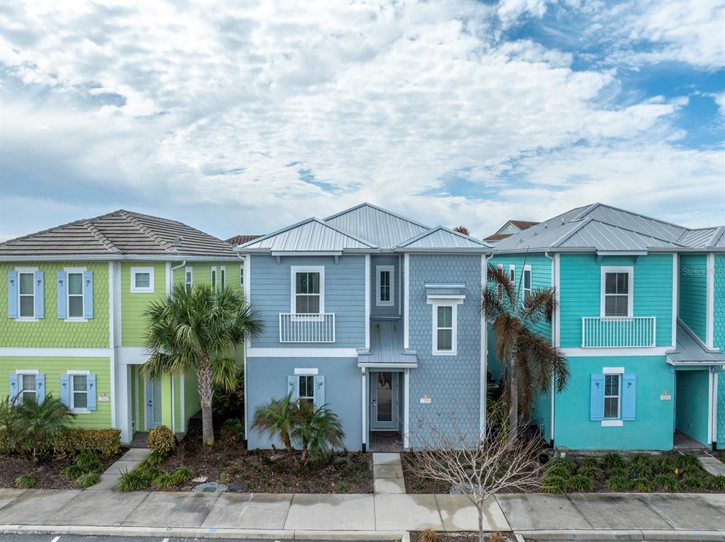 Three colorful, two-story houses with metal roofs stand side-by-side along a sidewalk — 7996 LOST SHAKER LANE, KISSIMMEE, FL