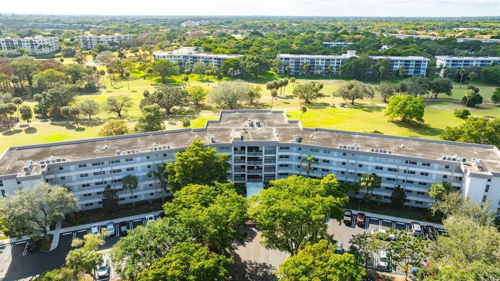 An aerial view shows a multi-story apartment building surrounded by a golf course and trees — 565 Oaks Lane # 103, Pompano Beach FL 33069, POMPANO BEACH, FL