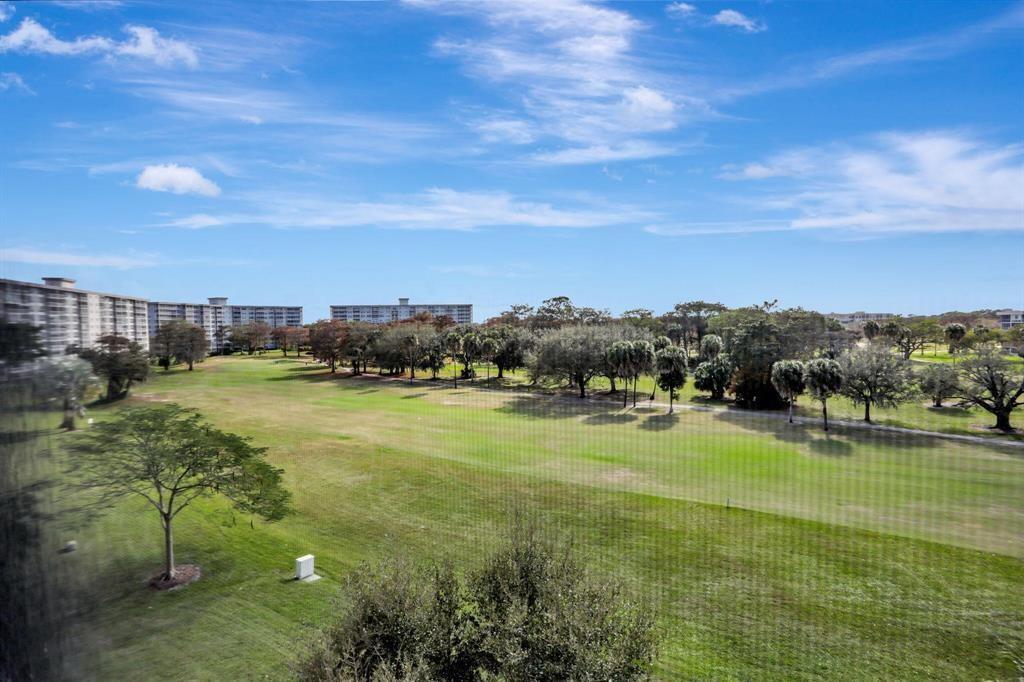A view of a grassy golf course with trees and apartment buildings under a blue sky — 565 Oaks Lane # 103, Pompano Beach FL 33069, POMPANO BEACH, FL