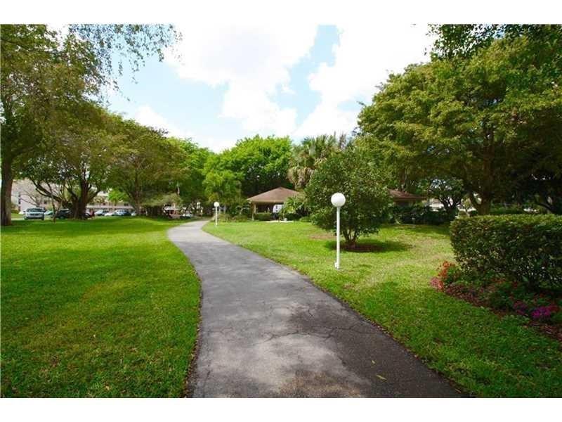 A paved walkway winds through a grassy park area with trees and a small gazebo — 565 Oaks Lane # 103, Pompano Beach FL 33069, POMPANO BEACH, FL