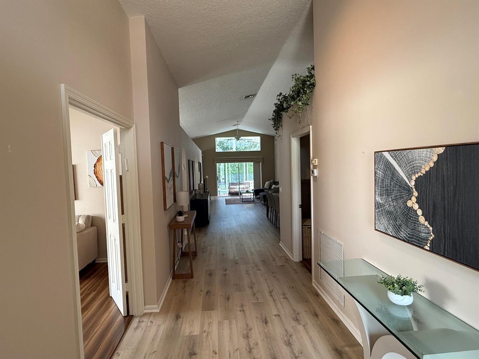 A hallway with light wood flooring leads toward a living area with vaulted ceilings — 5730 Royal Club Drive, Boynton Beach FL 33437, BOYNTON BEACH, FL