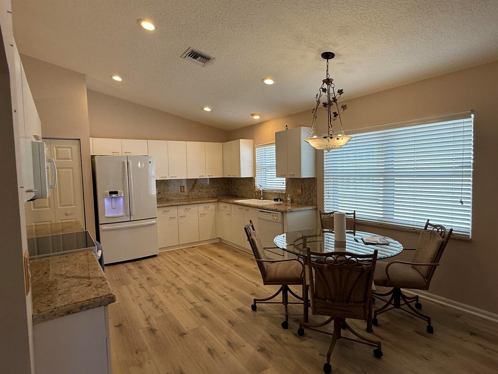 A kitchen features white cabinets, granite countertops, wood-look flooring, and a glass-topped dining table — 5730 Royal Club Drive, Boynton Beach FL 33437, BOYNTON BEACH, FL