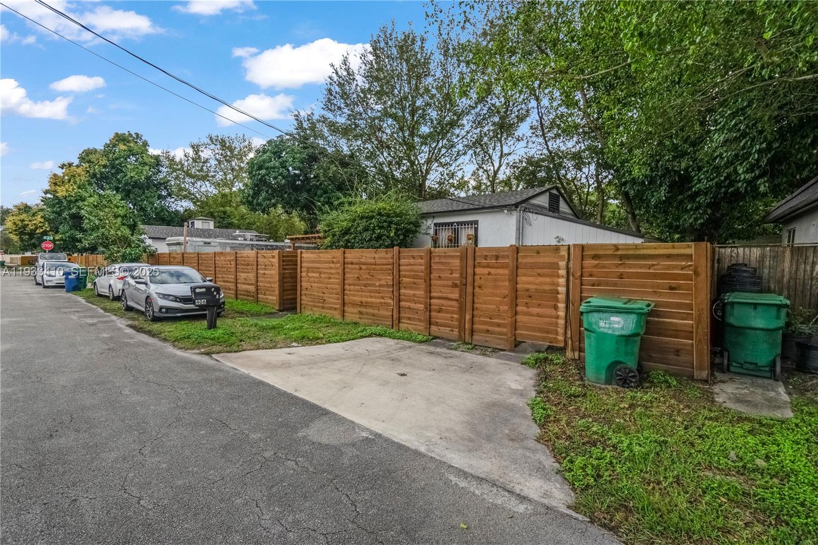 A wooden fence encloses a property with a concrete driveway and two green trash bins — 9210 NW 4th Ave, Miami FL 33150, MIAMI, FL