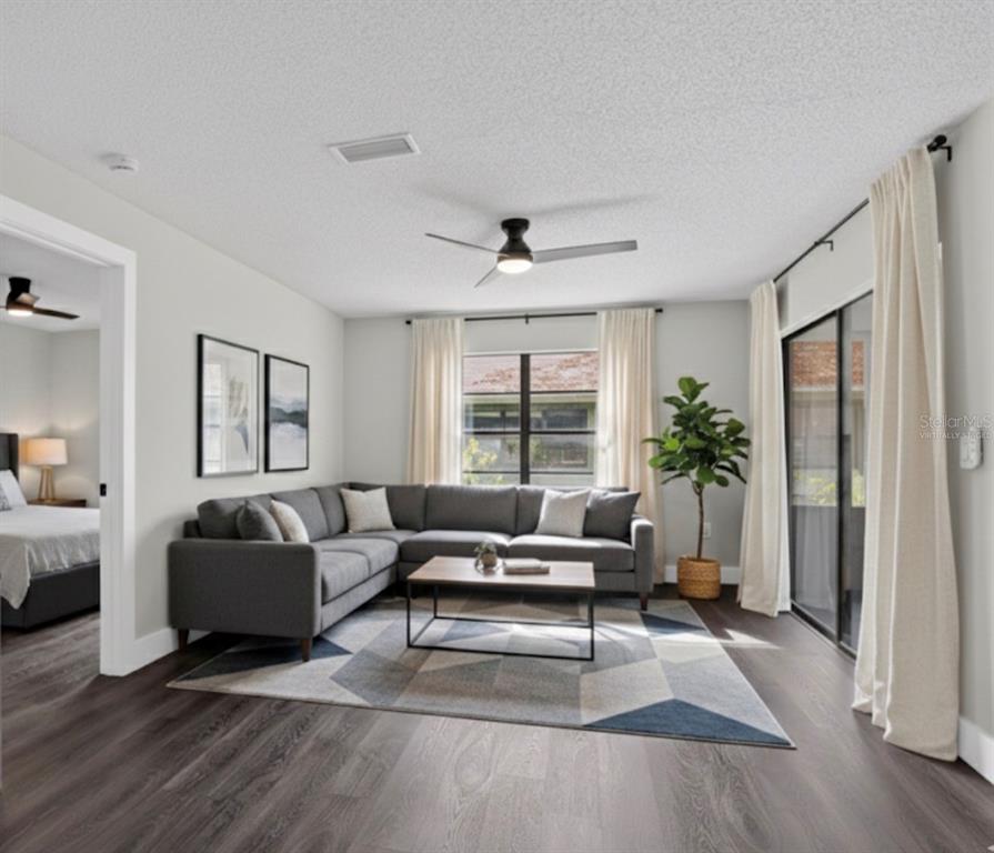 A living room features a gray sectional sofa, a geometric area rug, and dark flooring — 5014 BARRINGTON CIRCLE UNIT 2102, SARASOTA, FL