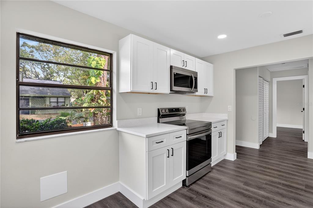 A kitchen features white cabinets, stainless steel appliances, and a window overlooking a wooded area — 5014 BARRINGTON CIRCLE UNIT 2102, SARASOTA, FL