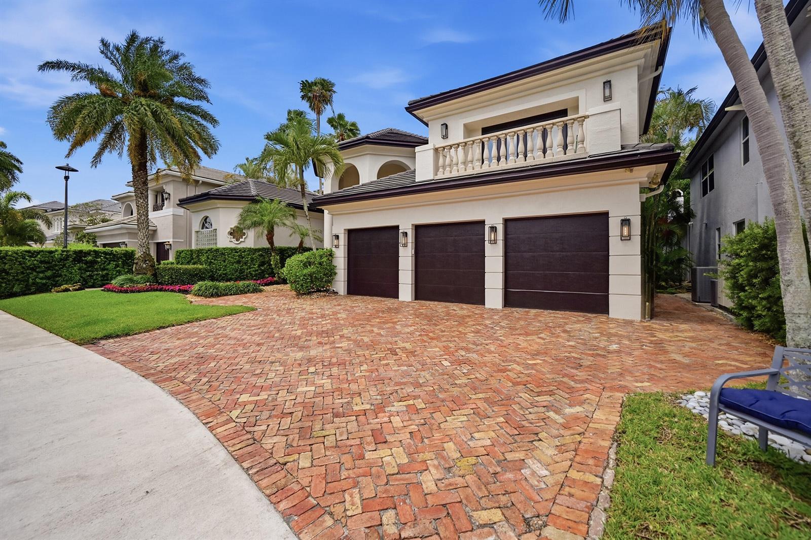 A three-car garage house with a brick driveway, balcony, and palm trees under a blue sky — 2425 NW 49th Lane, Boca Raton FL 33431, BOCA RATON, FL