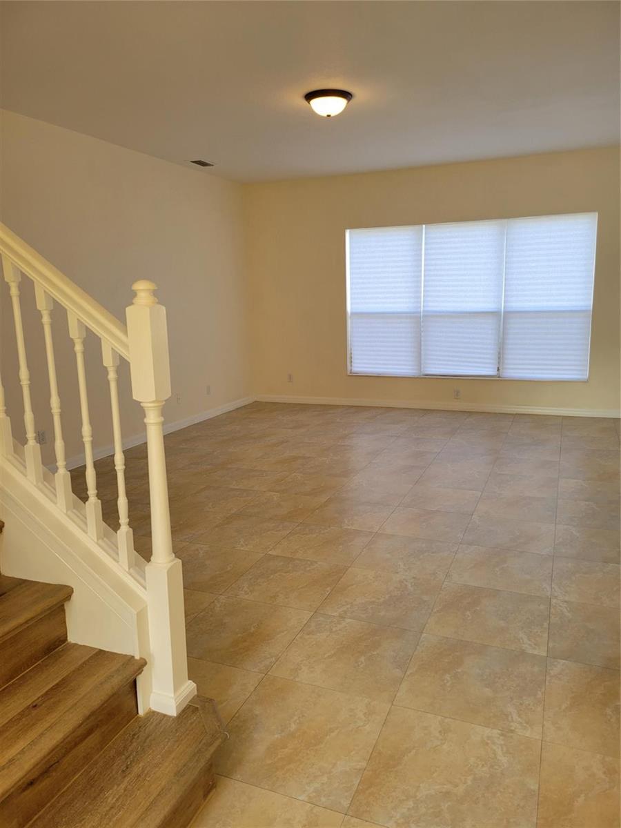 An empty room with beige tile flooring, cream walls, and a wooden staircase with railings — 8448 Adele Road, Lakeland FL 33810, LAKELAND, FL