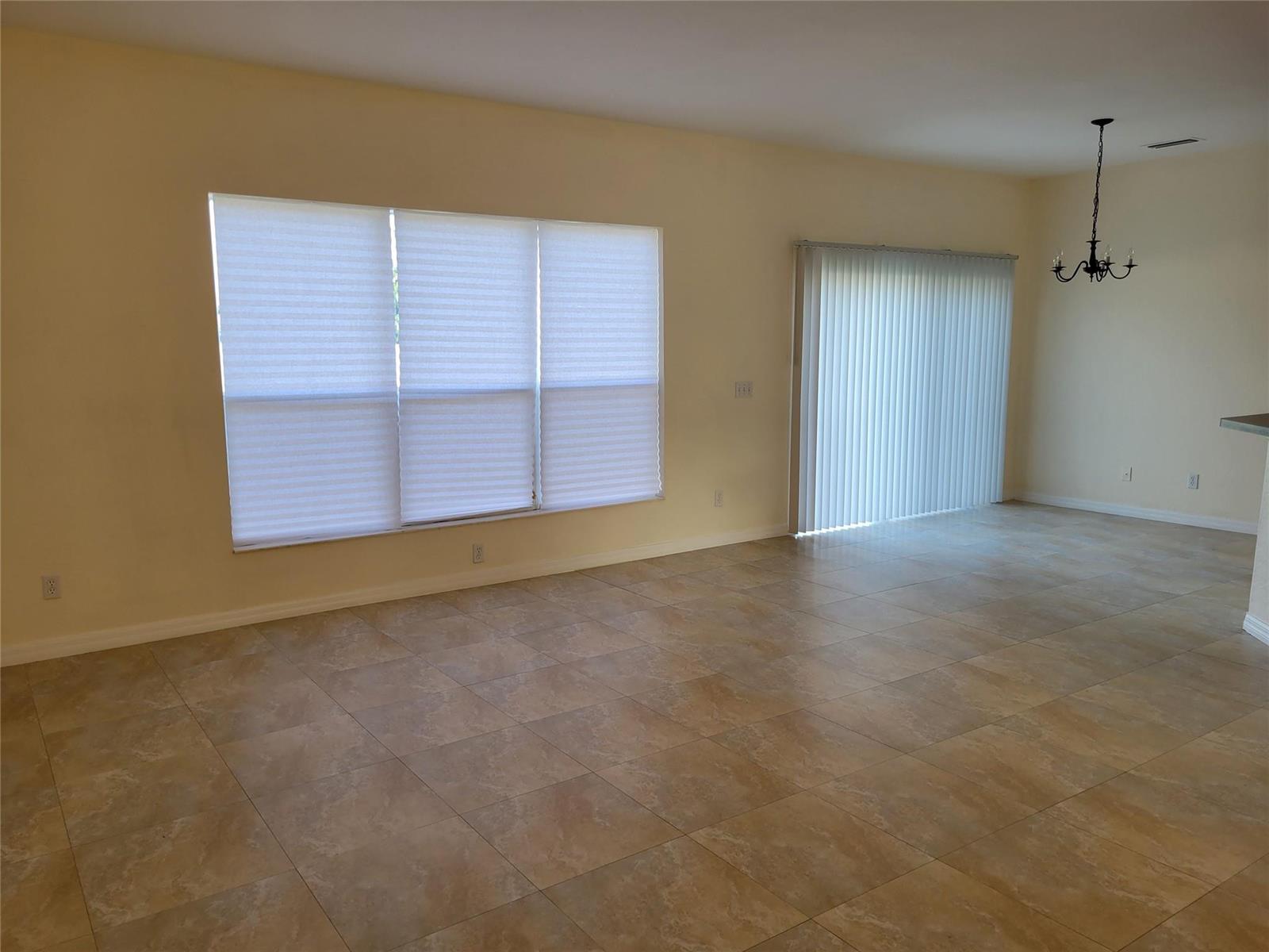 An empty room features beige walls, tile flooring, a large window, and sliding glass doors — 8448 Adele Road, Lakeland FL 33810, LAKELAND, FL