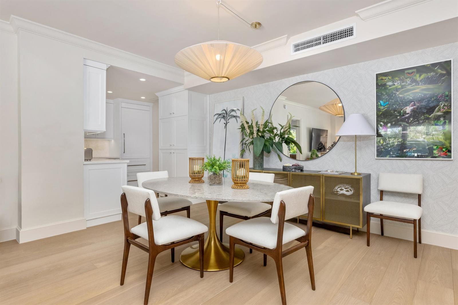 A dining room features a marble oval table, white chairs, and a large round mirror — 250 Bradley Place # 307, Palm Beach FL 33480, PALM BEACH, FL
