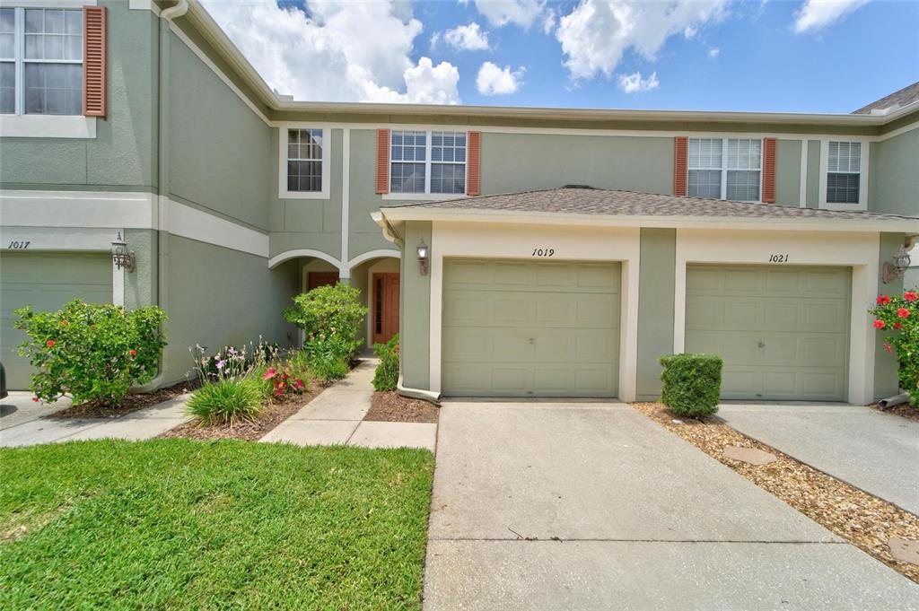 A row of three attached townhomes with green siding, beige trim, and individual garage doors — 1019 VISTA CAY COURT, BRANDON, FL