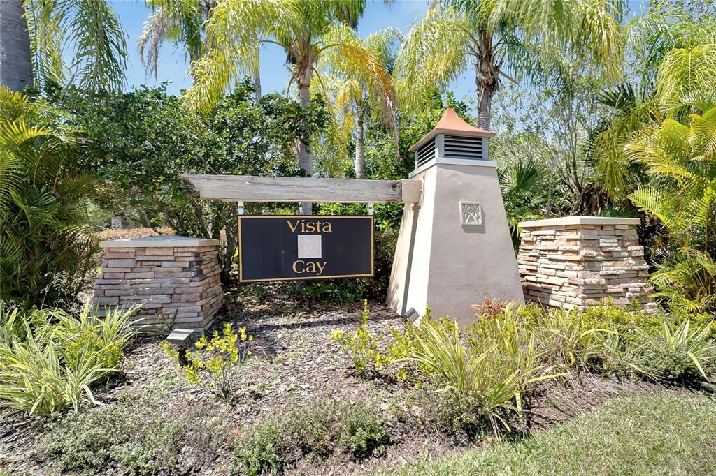 A stone and stucco monument sign for Vista Cay stands amidst tropical landscaping and palms — 1019 VISTA CAY COURT, BRANDON, FL