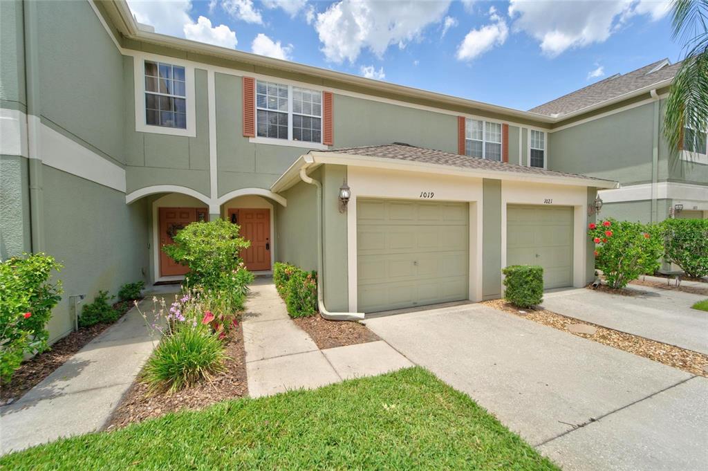A two-story townhouse exterior features green stucco walls, two garage doors, and landscaped front yards — 1019 VISTA CAY COURT, BRANDON, FL