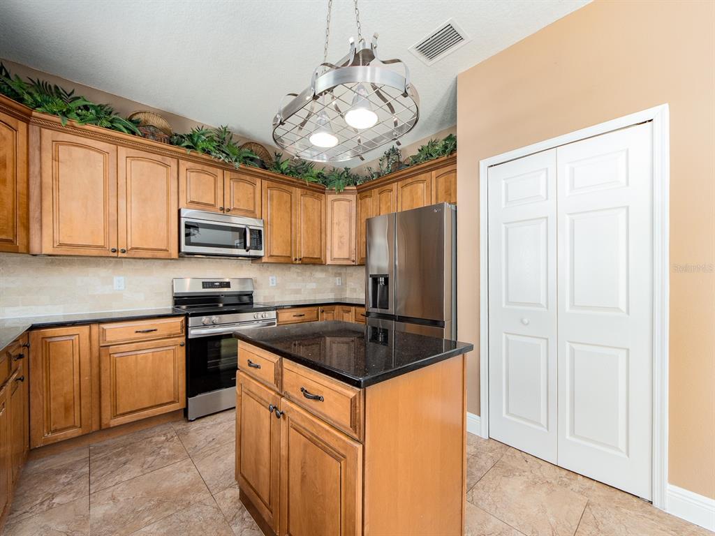 A kitchen features wood cabinets, black granite countertops, stainless steel appliances, and a central island — 3256 BENTLEY DRIVE, PALM HARBOR, FL
