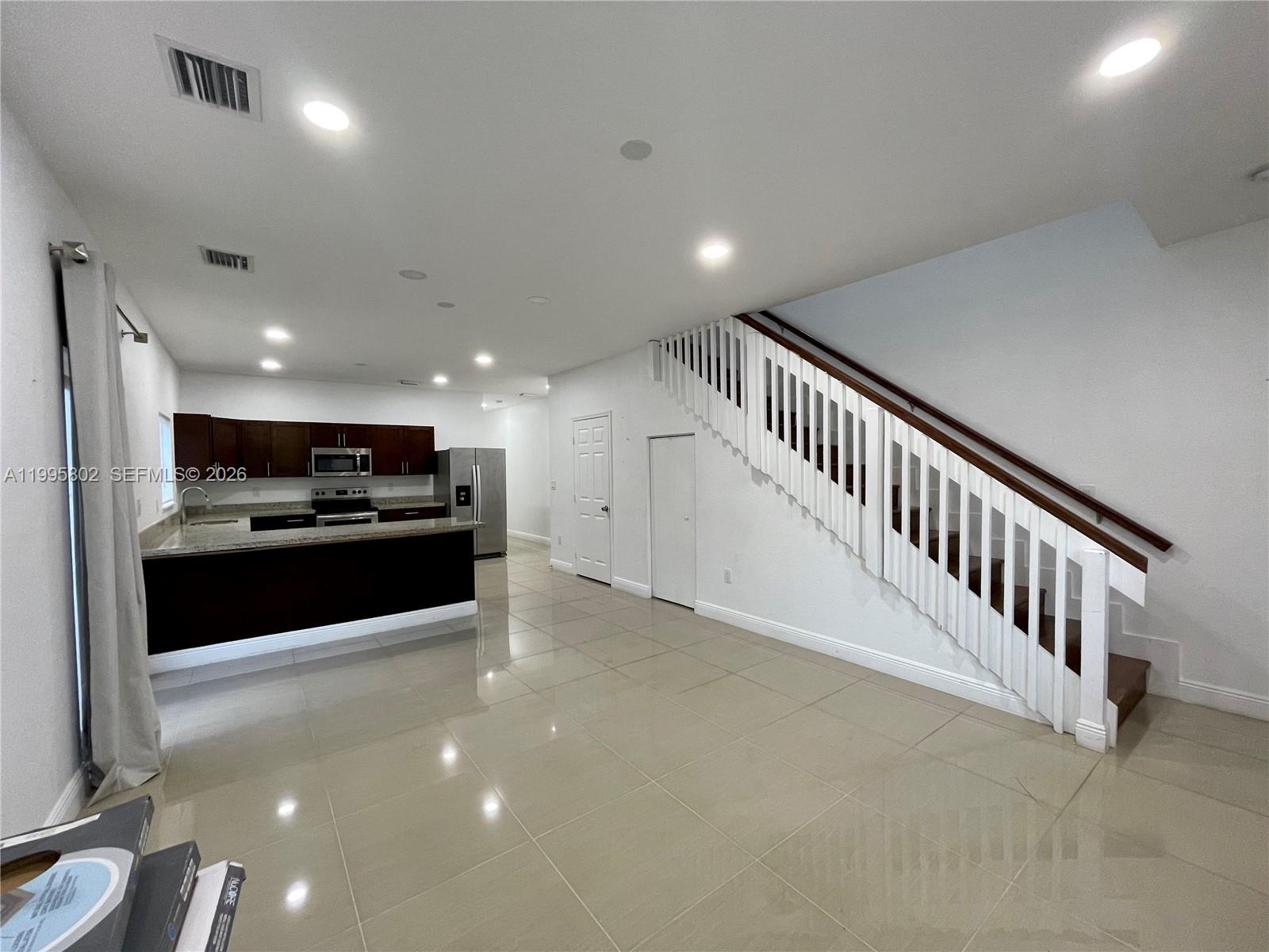 An open-concept kitchen with dark cabinets and tile flooring sits beside a white staircase — 1531 NW 55th Ter # 1533, Miami FL 33142, MIAMI, FL