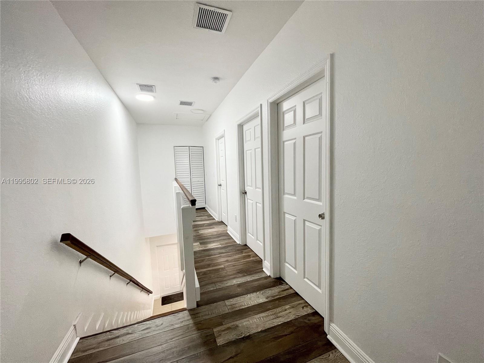 A hallway with wood-look flooring leads to several white doors and a staircase — 1531 NW 55th Ter # 1533, Miami FL 33142, MIAMI, FL