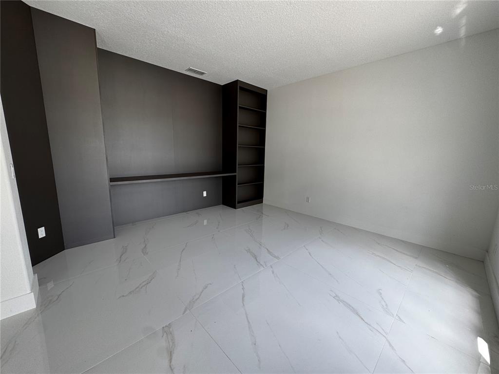 An empty room features white marble-look tile flooring and a dark built-in desk and shelving — 219 LARGOVISTA DRIVE, OAKLAND, FL