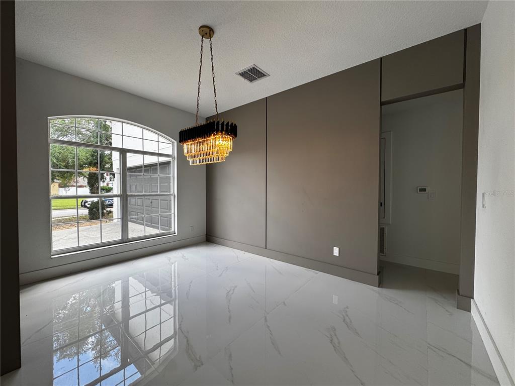 A dining room features white marble-look tile floors, a modern chandelier, and a taupe accent wall — 219 LARGOVISTA DRIVE, OAKLAND, FL